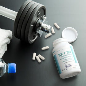 Capsules de Nurse Julli K2 + D3 à côté d'un verre d'eau