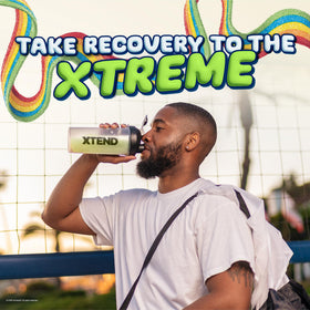 Poudre BCAA Xtend Original 30 Serv. Air Heads Rainbow Berry sur une table avec des accessoires de sport