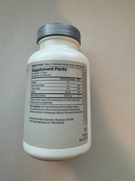 Shaklee Cholesterol Complex comprimés sur une table avec un verre d'eau